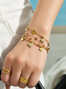 Primer plano de la pulsera dorada de varias capas con dijes de corazón brillantes.