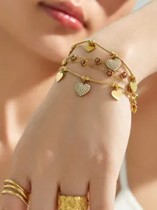 Primer plano detallado del brazalete de acero inoxidable bañado en oro con dijes de corazón.