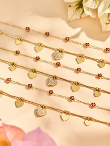 Vista detallada de la pulsera chapada en oro con dijes de corazón y rosa y circonitas brillantes.