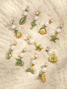 Detailansicht maritim gestalteter blauer Zirkon Perlen Ohrringe drapiert auf feinem Sandstrand.