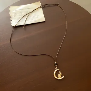 Detail shot of brown leather rope necklace featuring a gold crescent moon and cat pendant.