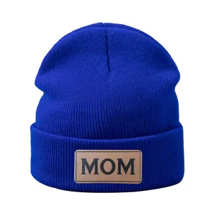 Gros plan détaillé d'un bonnet en tricot bleu roi avec écusson cuir marron texte.