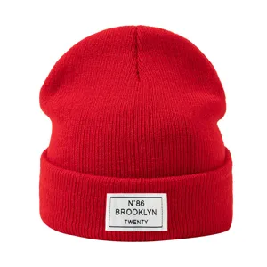 Gros plan sur les details du patch de bonnet en tricot rouge avec logo de lettres.
