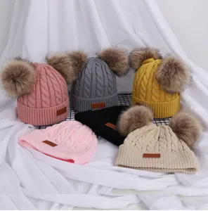Close-up view of children's double pom pom knit winter beanies featuring soft cable texture.