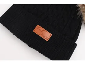 Black knitted winter beanie hat for kids with cozy faux fur pom pom and stylish leather logo patch.