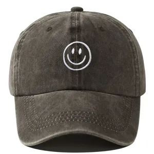Casquette de baseball noire délavée avec un joli visage souriant brodé blanc sur le devant.