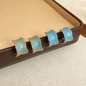 Primer plano detallado de pendientes de circonita en forma de C de oro y plata con piedras azules.