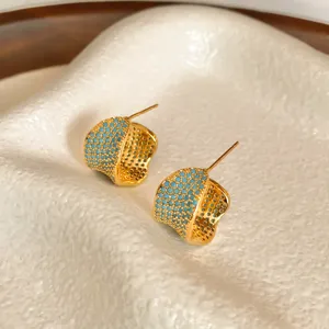 Exquisitos pendientes de botón dorados en forma de C con piedras micro-pavé azules, primer plano.