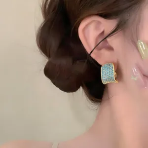 Primer plano de pendientes retro estilo corte, aretes anchos en forma de C con circonitas azules.