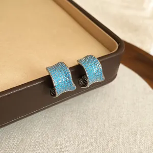 Primer plano detallado de pendientes de aro plateados con pavé de circonitas azules brillantes.