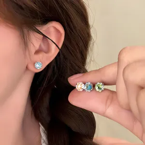 Close-up detail of stylish round colored zircon stud earrings worn on ear and held in hand.