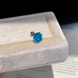 Detailed close-up of a vibrant blue zircon stud earring placed on a soft velvet jewelry box.