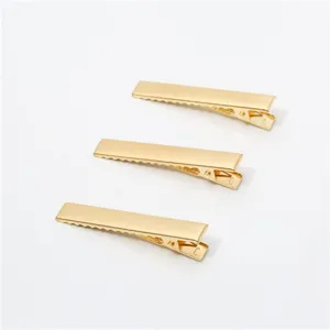 Detail shot of three golden metal duckbill hair clips, showing smooth surface and teeth.