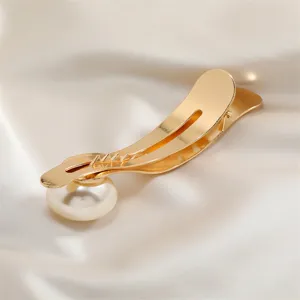 Close-up detail of a golden metal hair clip featuring an elegant faux pearl decoration.