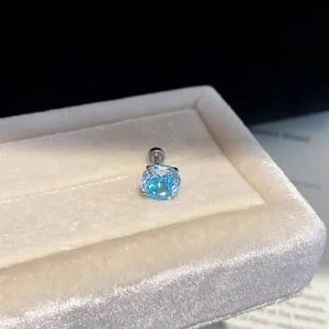 Close-up detail view of a sparkling light blue zircon stud earring on soft beige velvet box.
