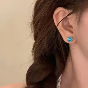 Close up detail of a sparkling blue round zircon stud earring worn on ear, minimalist fashion jewelry detail.
