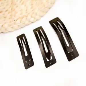 Primo piano di tre fermagli per capelli a scatto in metallo nero di varie dimensioni e stile.