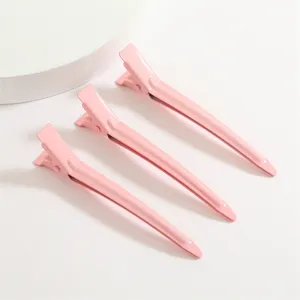 Gros plan de trois pinces à cheveux bec de canard en aluminium rose avec finition laquée.