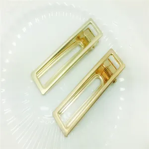Gold hollow rectangular hair clip detail shot, showing metal texture and spring mechanism.