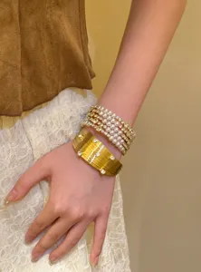 Gros plan détail de bracelet manchette doré et perles multicouches vintage au poignet.