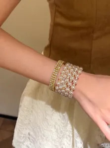 Détail en gros plan d'un bracelet empilé doré en perles multicouches et strass.