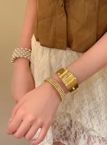Détail de bracelets superposés dorés vintage, large manchette élégante et perles.