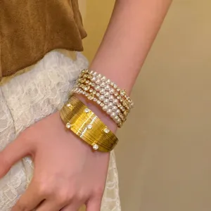 Détail de bijoux de bracelets superposés en perles vintage et manchette dorée texturée.