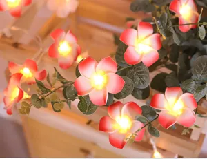 Detalle de luces LED de plumeria cálidas con hojas verdes para una decoración de habitación acogedora.