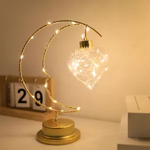 Crescent moon LED night light with hanging heart bulb, warm ambient table lamp for bedroom decor.