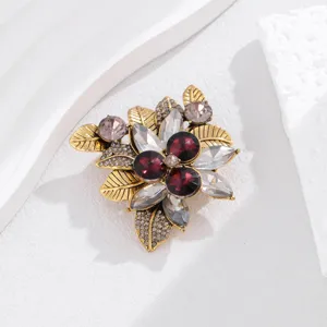 Vintage crystal flower brooch closeup, sparkling red rhinestones and gold leaf details.