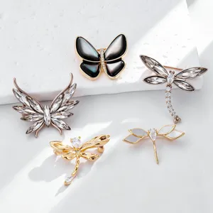 Closeup detail of crystal butterfly and dragonfly brooches on white display, elegant pins.