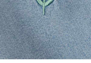 Primo piano dettagliato di tessuto denim blu per bambini con delicato ricamo verde.