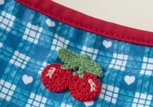 Close-up of cute cherry embroidery and blue plaid fabric on children's swimsuit detail.