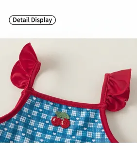 Kids swimsuit detail view, blue plaid pattern with sweet cherry embroidery and cute ruffle straps.