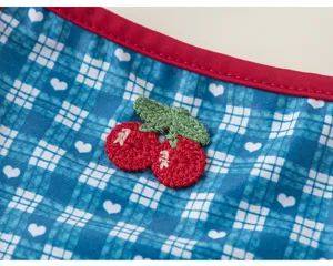 Detailed view of girls one-piece swimsuit featuring blue plaid heart print and crochet cherry.