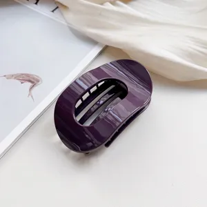Detail shot of a sleek dark purple oval hair claw clip, elegant minimalist design for secure styling.