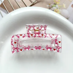 Detail view of a clear square hair claw clip featuring sweet pink bows and red heart prints.