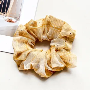 Detail of chiffon hair scrunchie with rhinestones sparkling on yellow sheer fabric texture.