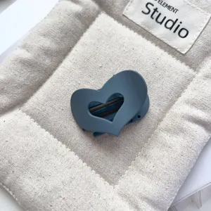 Close-up detail shot of a matte blue heart cutout hair claw clip on a textured fabric.