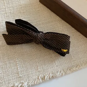 Close-up detail of a brown polka dot hair bow clip with a metallic tag on textured fabric.