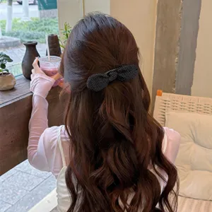 Detailed view of a chic black polka dot bow hair clip styling on long brown wavy hair.
