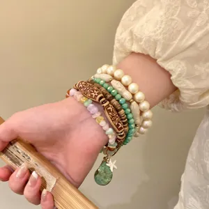 Close-up detail of forest style stacked beaded bracelets with pearls, carved wood and stone charms.