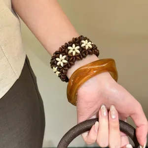 Bracelet de perles fleur bohème et large jonc en résine acrylique portés au poignet.