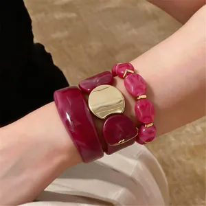 Close-up detail of burgundy acrylic resin and gold-tone metal spliced elastic bracelet.
