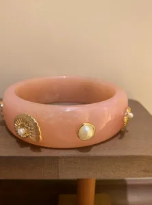 Close-up of pink resin chunky bangle featuring gold shell and pearl details for style.
