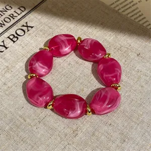 Close-up detail of hot pink marbled acrylic and gold metal beaded stretch bracelet.