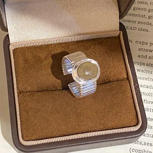 Bague ouverte en métal chic avec anneau rayé et pierre centrale lisse, vue de détail élégante.