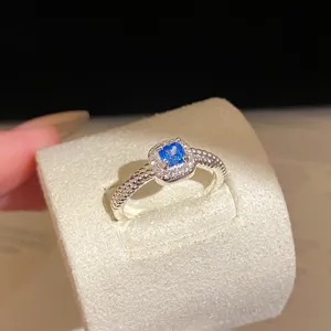 Vue rapprochée détaillée de la bague étincelante à pierre bleue carrée avec anneau perlé.