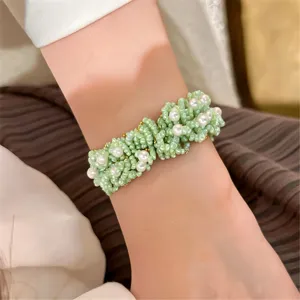 Detalle de pulsera tejida con rocallas verdes y perlas, joya de muñeca elegante y estilizada.
