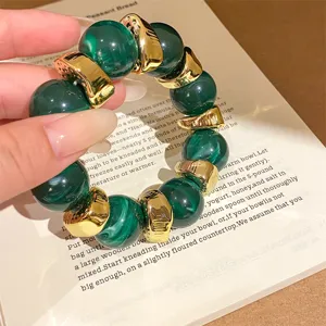 Detailed shot of dark green textured resin and gold bead bracelet, edgy trendy luxury style.